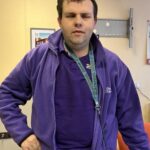 Photograph of Peter looking towards the camera. He is wearing a purple Disability Equality top.
