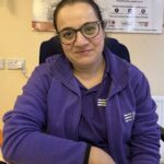 Photograph of Shamim looking towards the camera. She is wearing a purple Disability Equality top.