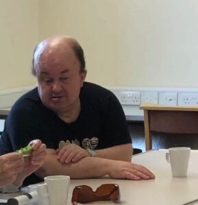 Photo of David talking to someone out of shot, sharing knowledge with a focused face. A set of cups around them on a desk. 