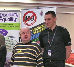 Photo of David and PC ASH on a DENW stall, with HateCrime banners in the background. 