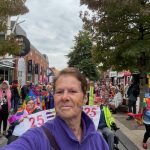 Our CEO Mel Close taking a selfie on the main shopping strip in Preston. Behind her the team are holding the 25 years of DENW banner and travelling along the road together.