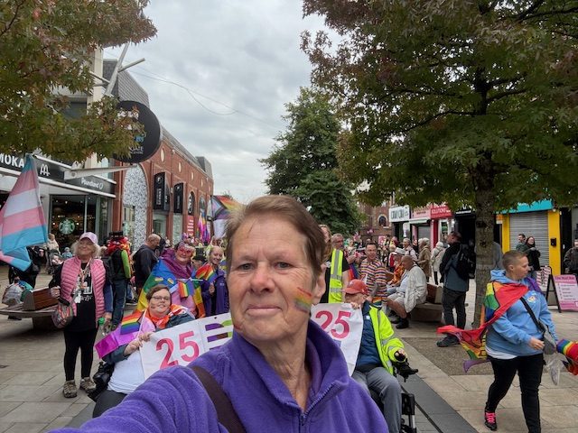 Our CEO Mel Close taking a selfie on the main shopping strip in Preston. Behind her the team are holding the 25 years of DENW banner and travelling along the road together.