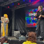 Live shot of stage with presenter and BSL interpreter to the side of the artist signing.