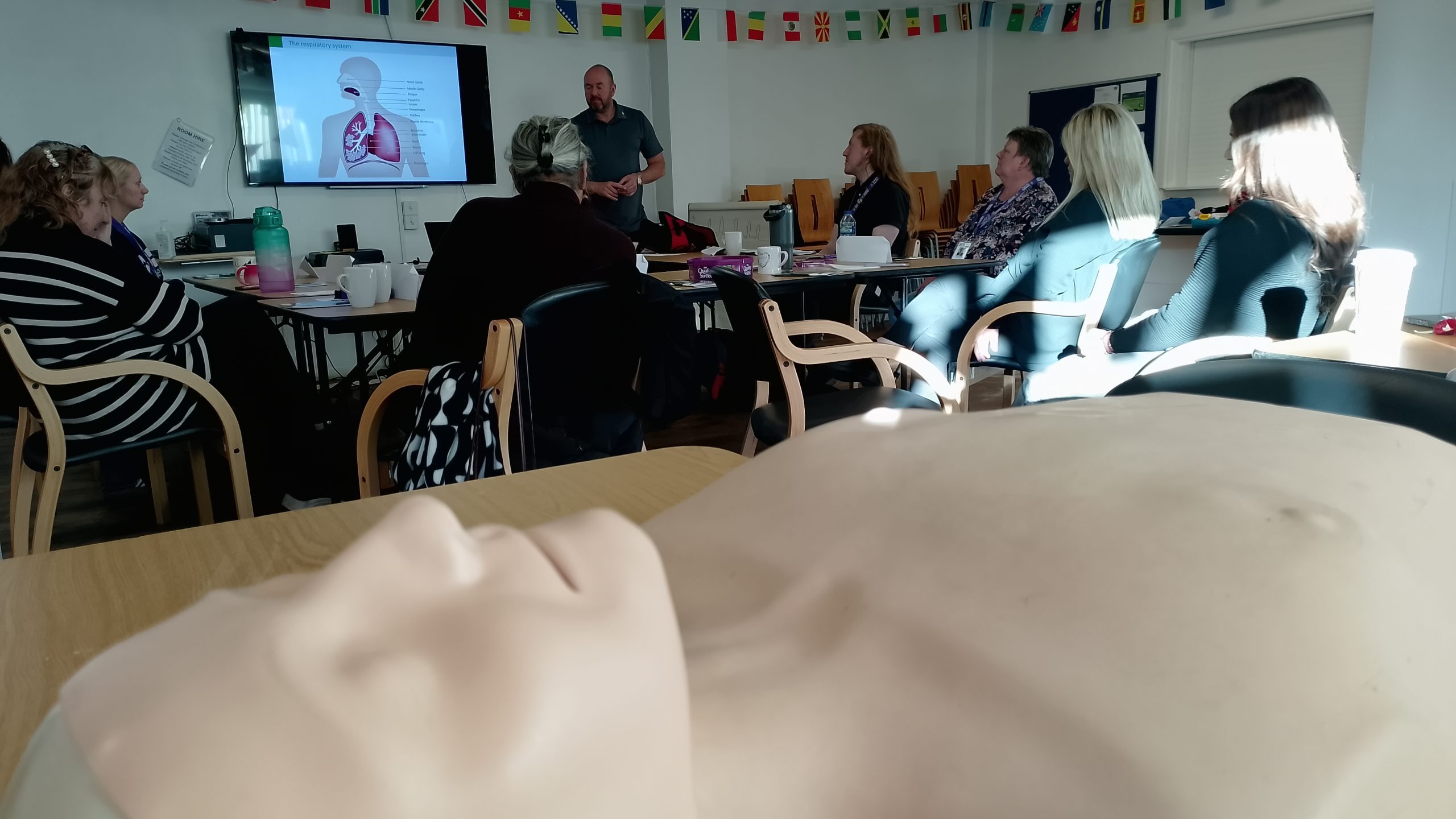 Foreground shot of Annie the resuscitation dummy with the group training course in the background.